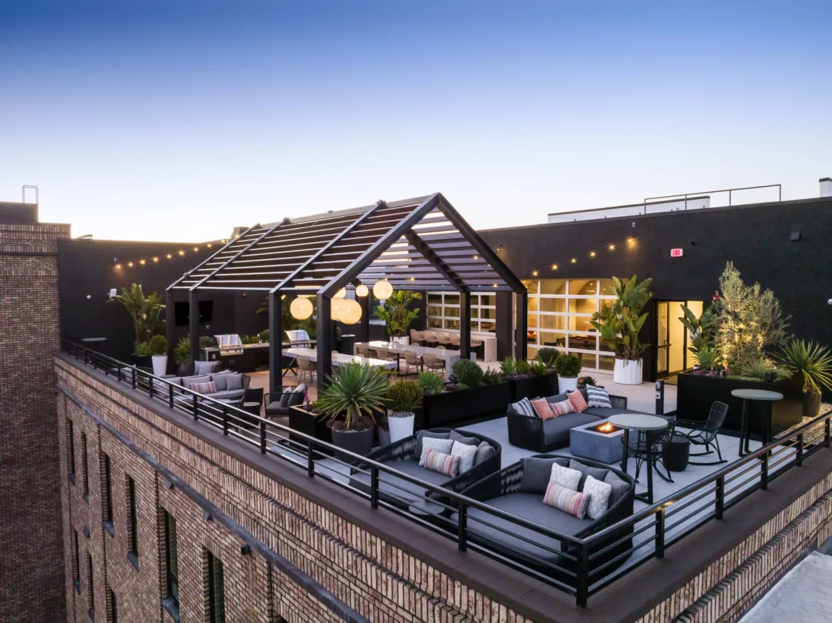 Rooftop lounge with lounge seating and bar under a pergola with hanging lights.