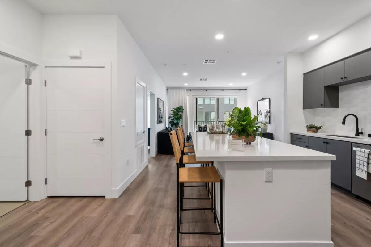 A kitchen with wood-style flooring, white walls, and kitchen island with high yellow chairs.