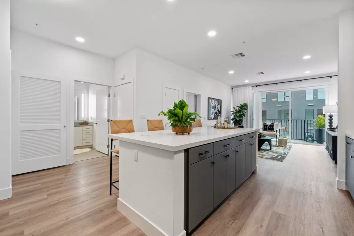 A kitchen with wood-style flooring, white walls, and kitchen island with high yellow chairs.