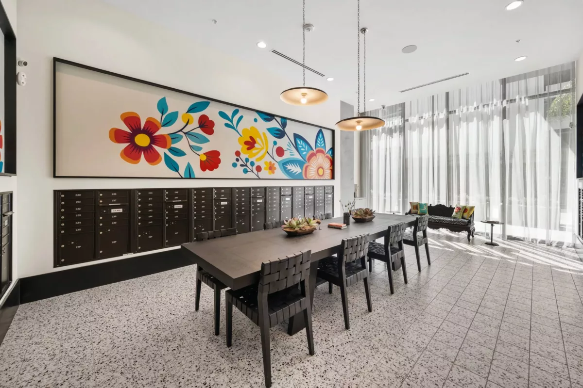 Mailroom with long table in the center with chairs, black mailboxes in the walls, and bright floral artwork.