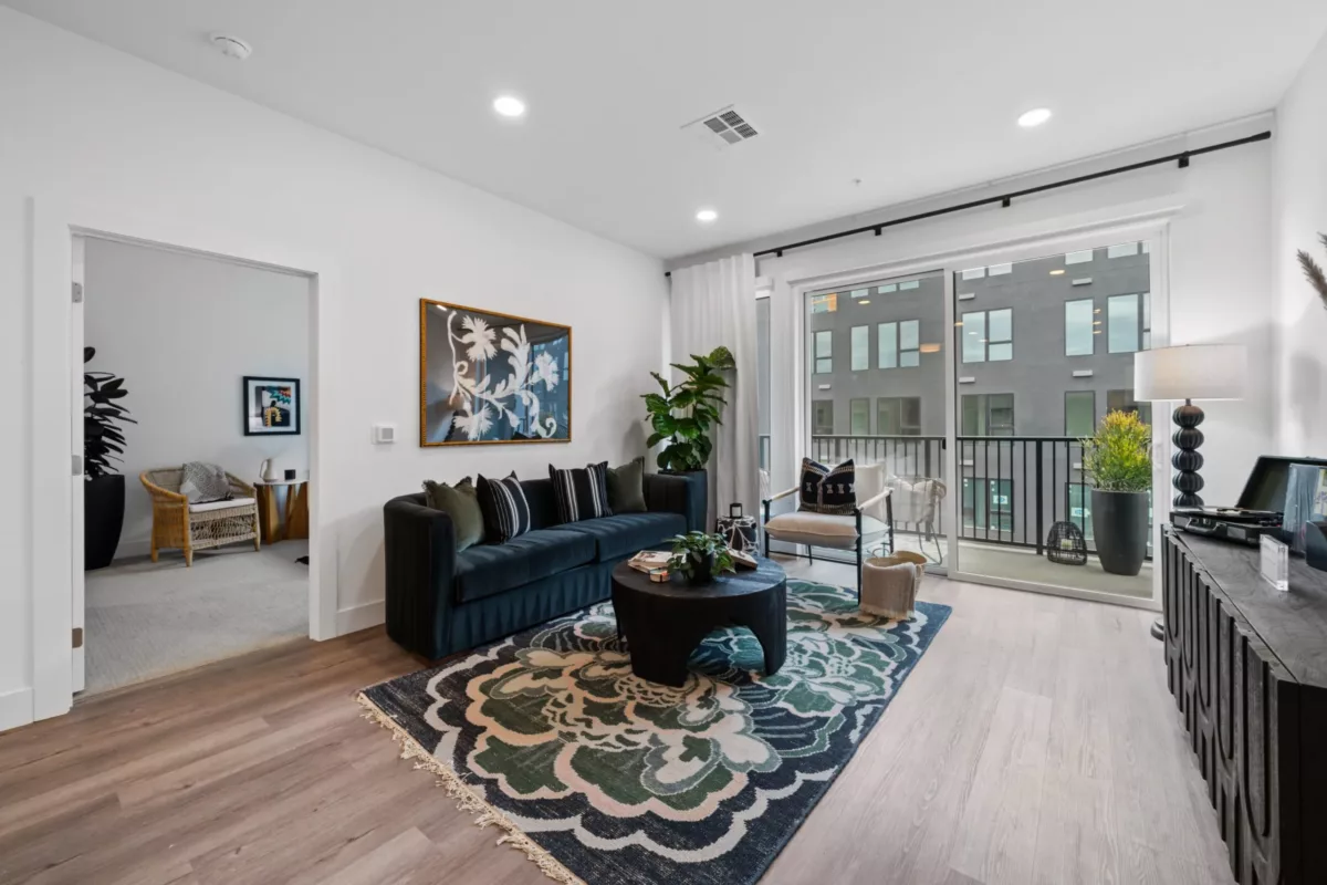 A living room with wood-style flooring, dark blue couch, modern art on the wall, and a large window.