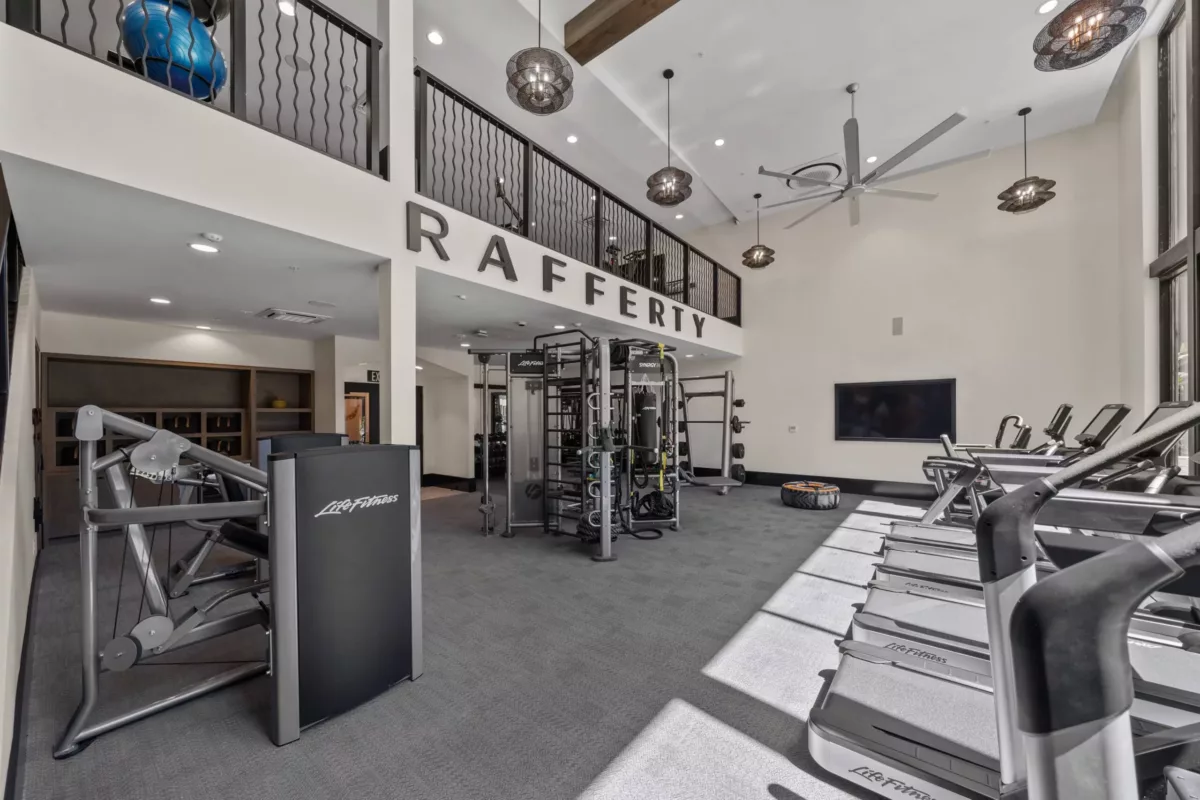 Two-story fitness center with cardio equipment and colorful mural on the far wall