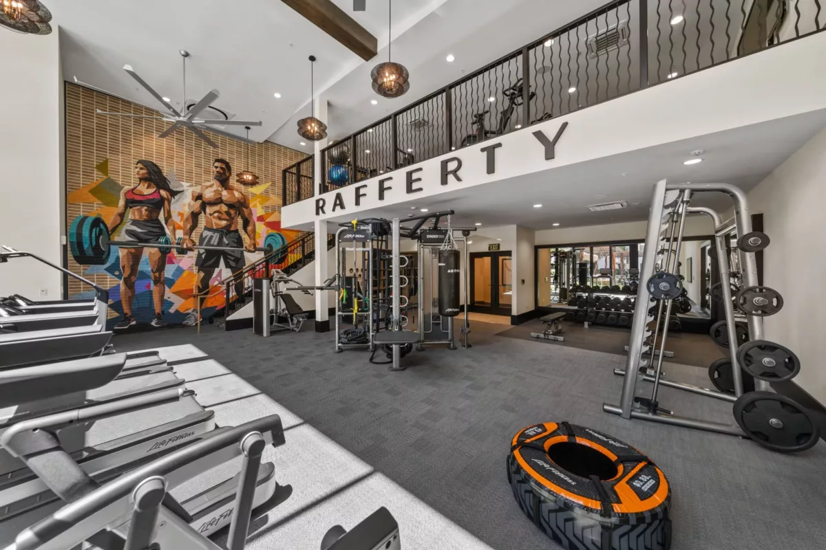 Two-story fitness center with cardio equipment and colorful mural on the far wall