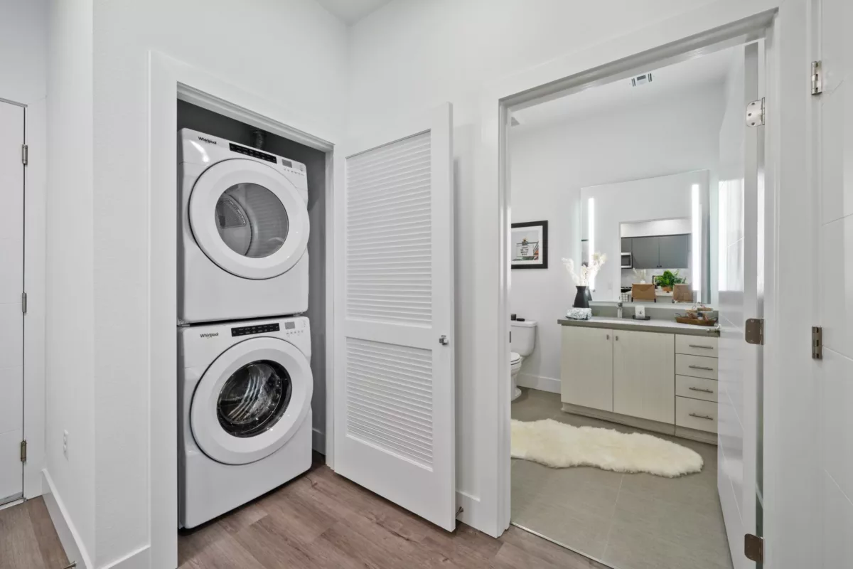 Closet with an open door that reveals a stacked washer and dryer, next to the doorway to a bedroom.