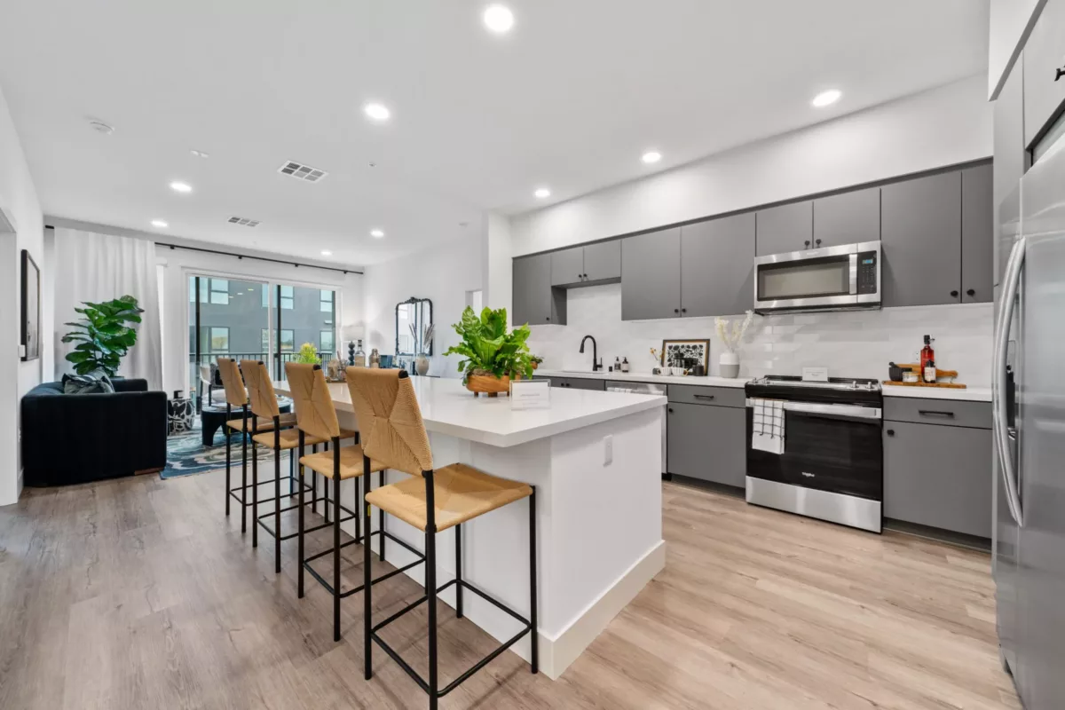 A kitchen with wood-style flooring, kitchen island with high chairs, gray cabinets, and stainless steel appliances.