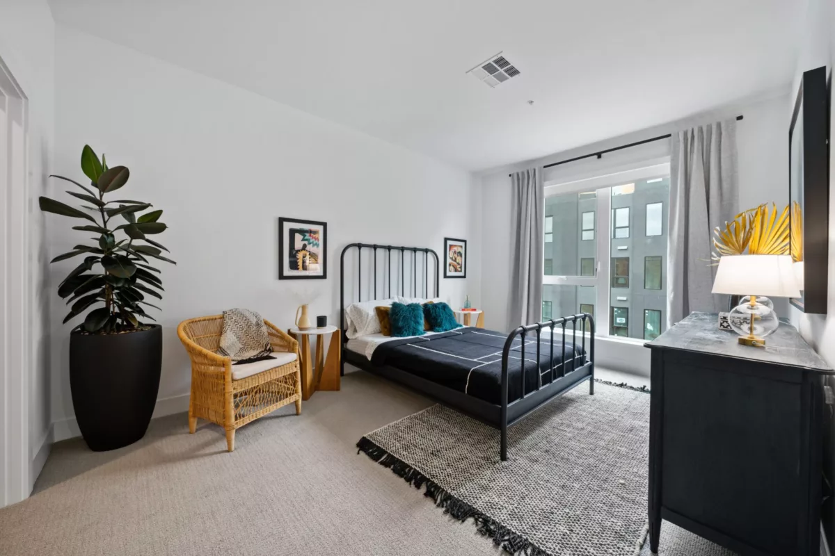 A bedroom with a bed with metal frame, white walls, and a large window.