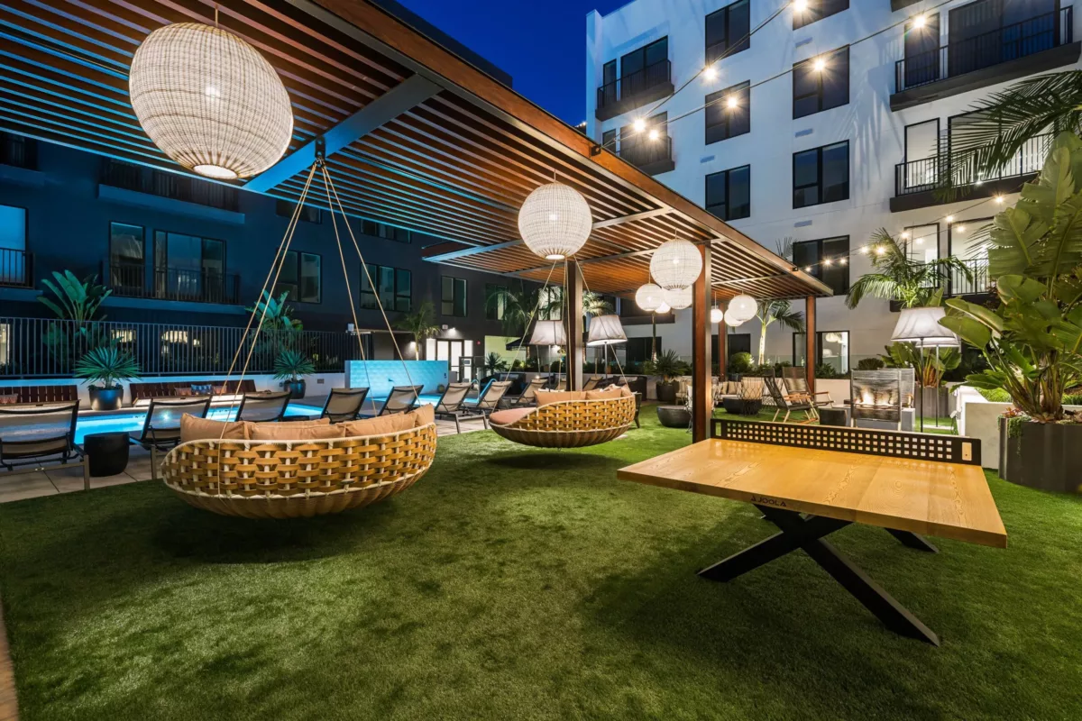 Outdoor lounge with large hanging circular chairs beneath a pergola and hanging lights.
