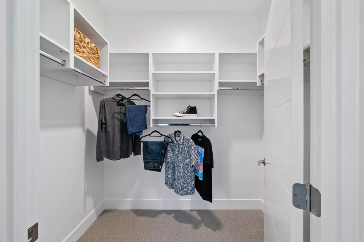 A large closet with built-in white shelving with clothing hanging.
