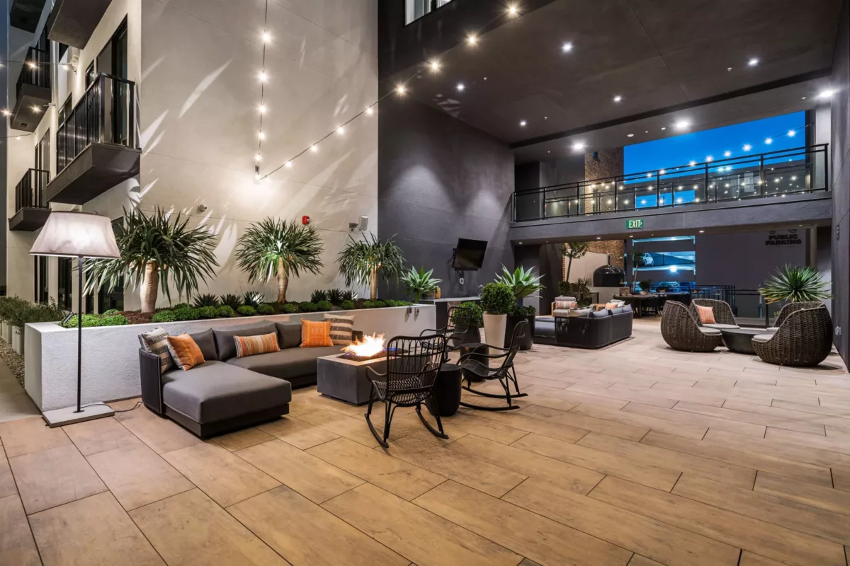 Outdoor lounge with couches and firepit beneath string lights.