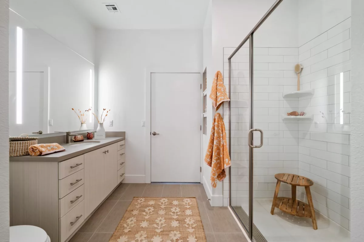 A bathroom with light-colored vanity and a mirror and a glass-enclosed shower stall.