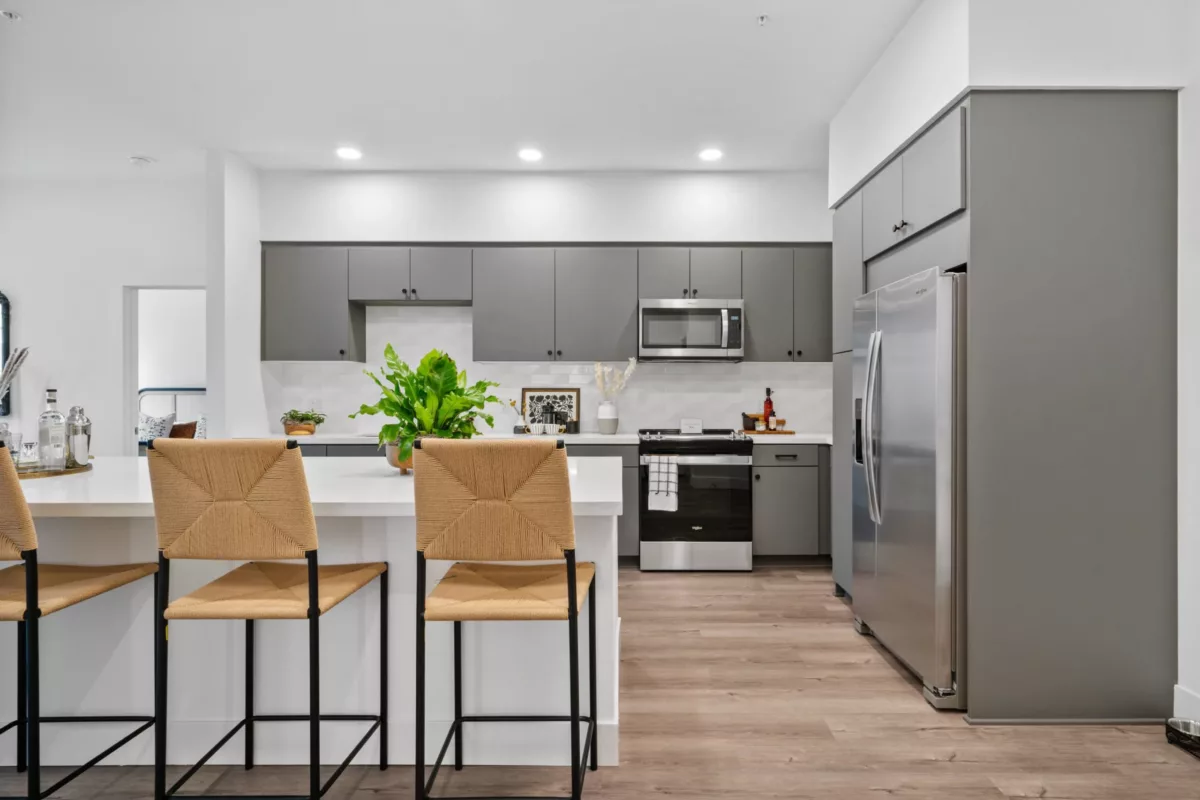 A kitchen with wood-style flooring, kitchen island with high chairs, gray cabinets, and stainless steel appliances.