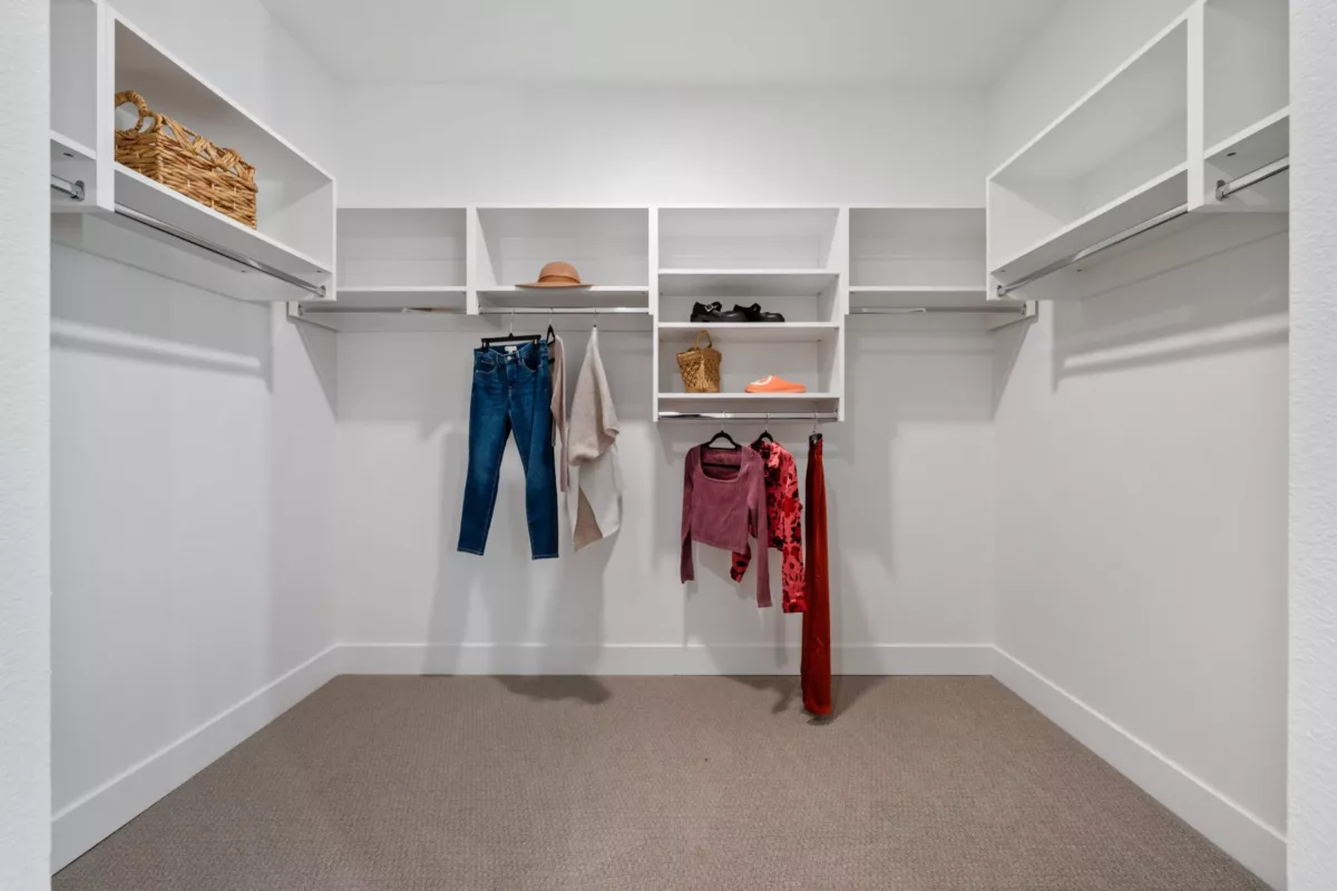 A large closet with built-in white shelving and clothes hanging.