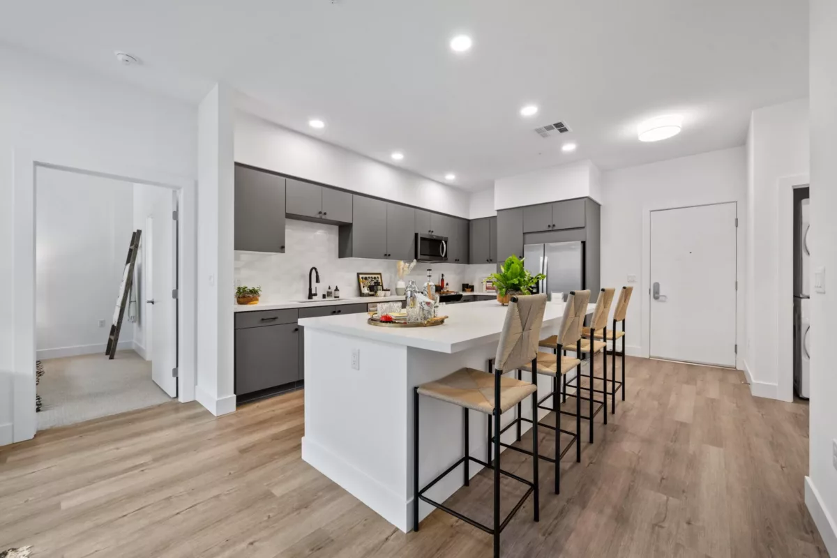 A kitchen with wood-style flooring, kitchen island with high chairs, gray cabinets, and stainless steel appliances.