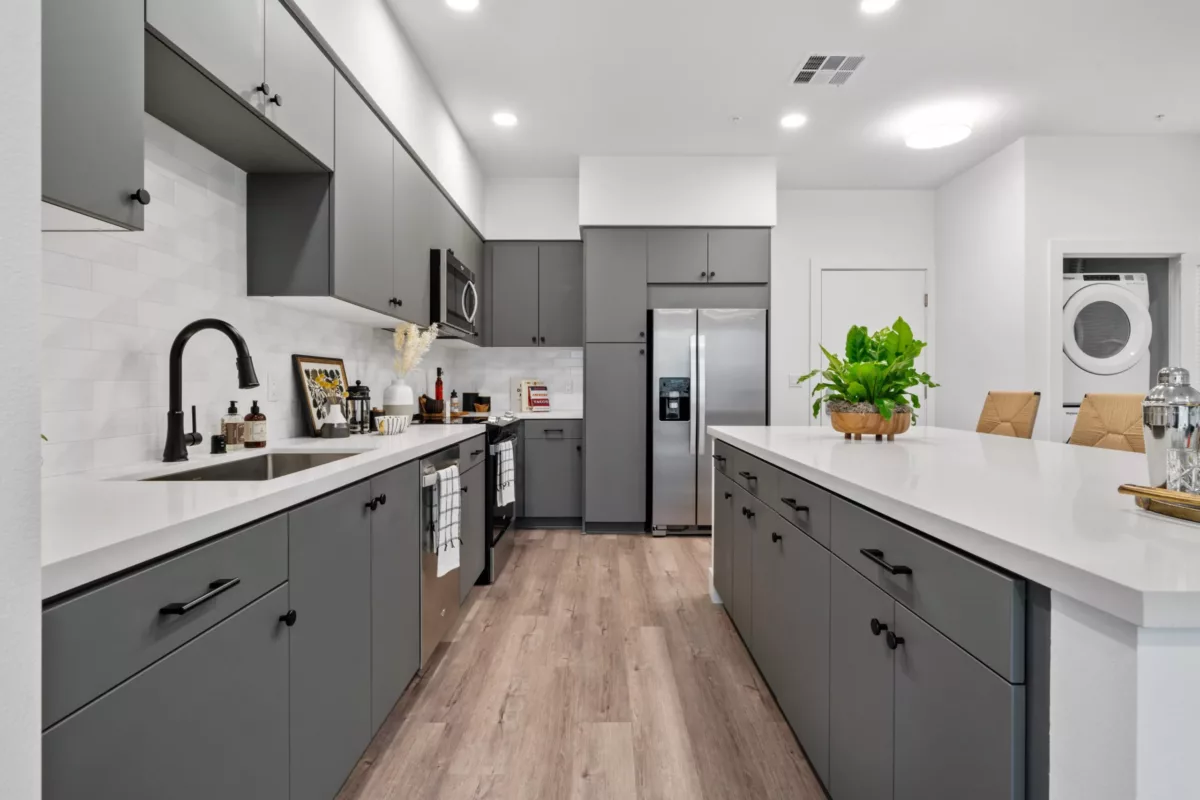 A kitchen with wood-style flooring, kitchen island, gray cabinets, white tile backsplash,and stainless steel appliances.