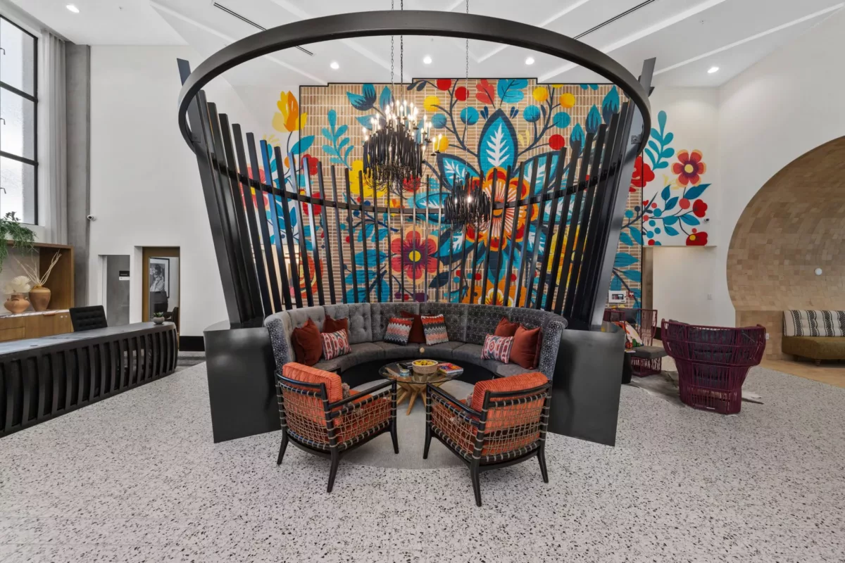 A lounge with a gray couch, red chairs, a large curved dividing wall with basket-like slats, and a floor-to-ceiling floral mural on the wall in the background.
