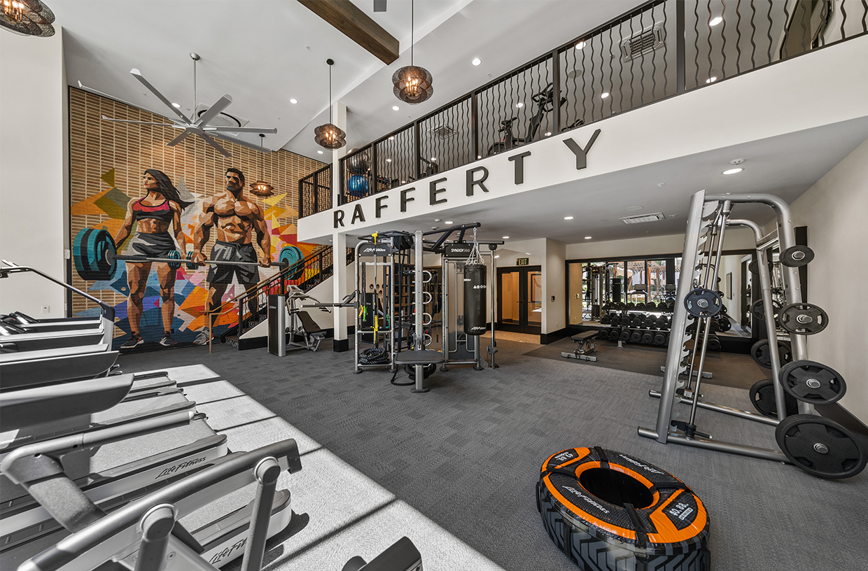 Two-story fitness center with cardio equipment and colorful mural on the far wall